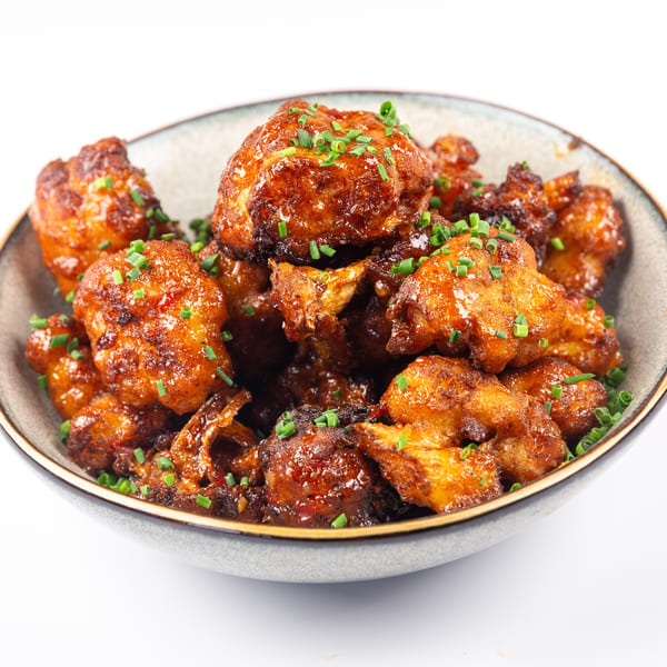 Bowl of crispy fried cauliflower bites coated in a glossy sauce and topped with chives.