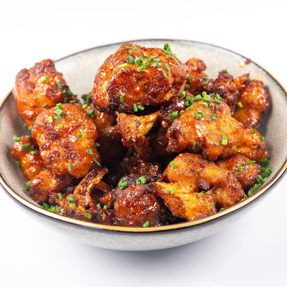 Bowl of crispy fried cauliflower bites coated in a glossy sauce and topped with chives.