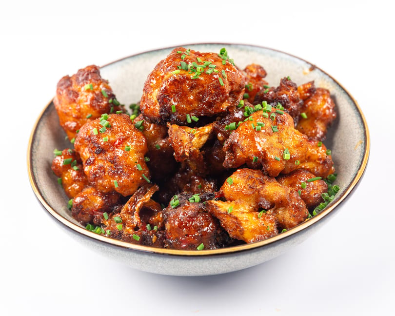 Bowl of crispy fried cauliflower bites coated in a glossy sauce and topped with chives.