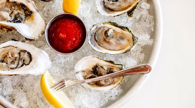 Fresh oysters on a bed of ice with cocktail sauce, lemon wedges, and an oyster fork.