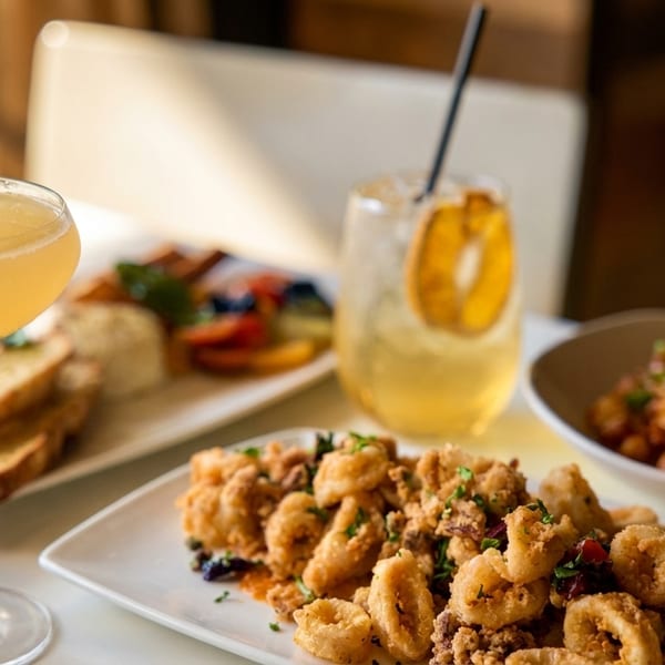 A table laden with fried calamari, pasta, and two cocktails, one with a lemon twist.