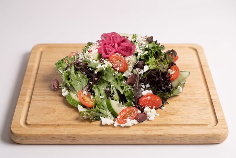 Fresh garden salad with mixed greens, tomatoes, cucumbers, feta, olives, and pickled red onions.
