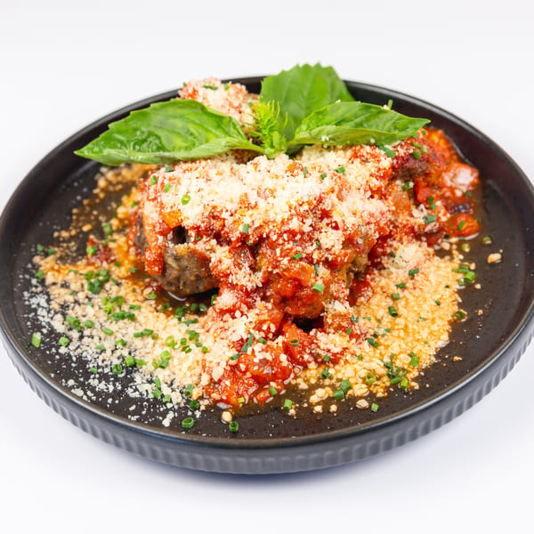 Meatballs covered in red sauce, grated cheese, basil, and chives on a dark plate.