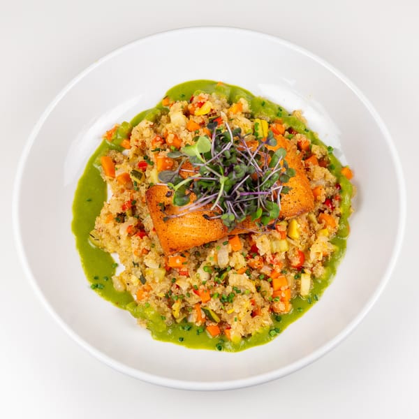 Crispy salmon fillet on vegetable quinoa with vibrant green sauce and fresh microgreens.