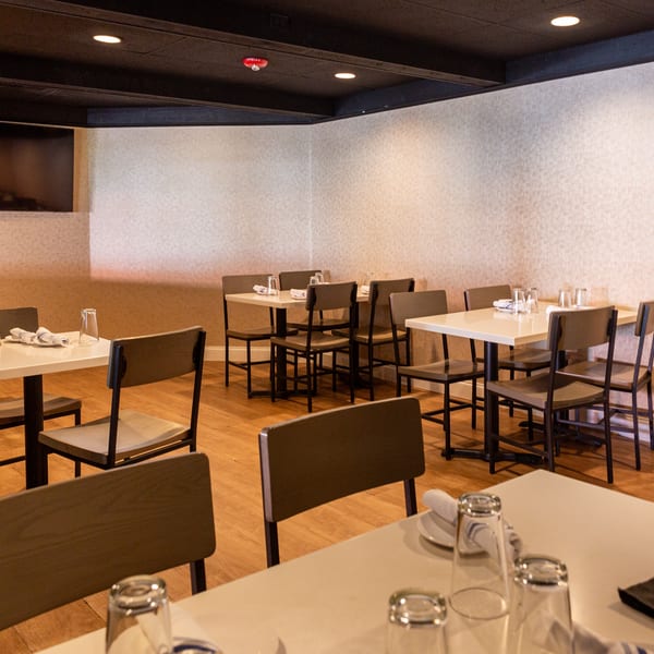 Spacious restaurant dining room with neatly set tables, chairs, and a large screen on the wall.