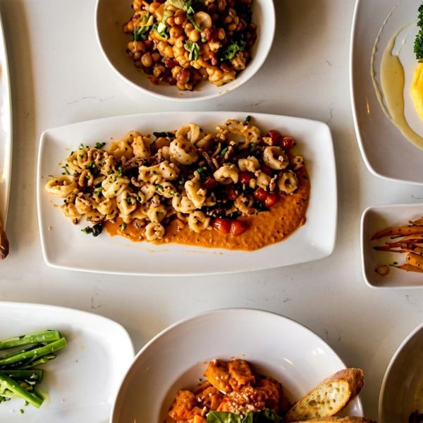 Overhead view of various Italian dishes, including pasta, burrata, salmon, and vegetables on a white table.