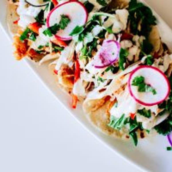 Three vibrant tacos with radish, cabbage, and cilantro on a white platter.