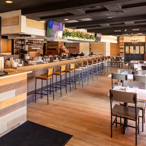 FORAGE restaurant interior with a long bar, dining tables, wood accents, and TV screens showing sports.