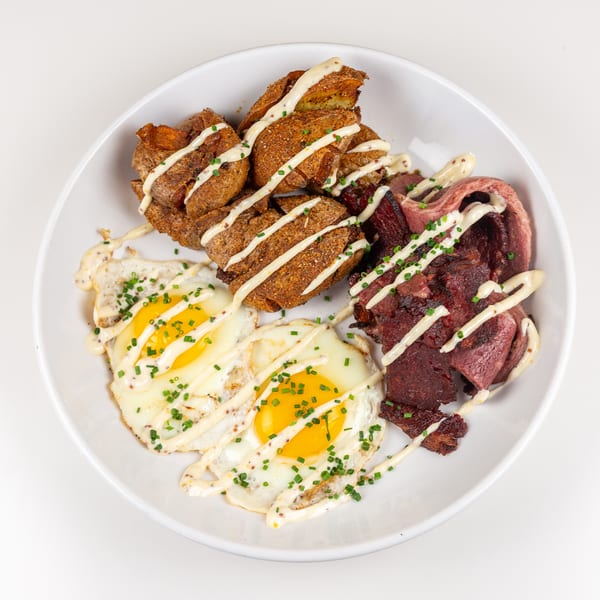 Two fried eggs, roasted potatoes, and sliced beef, drizzled with creamy sauce and chives.