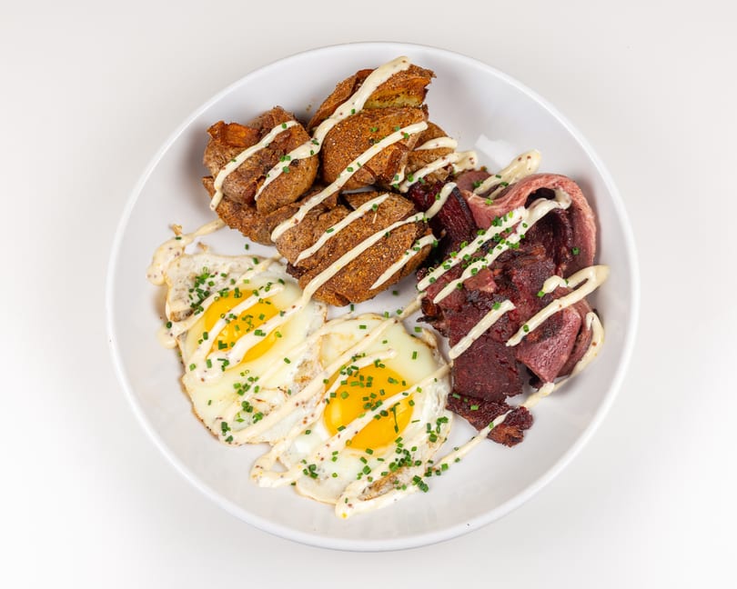 Two fried eggs, roasted potatoes, and sliced beef, drizzled with creamy sauce and chives.